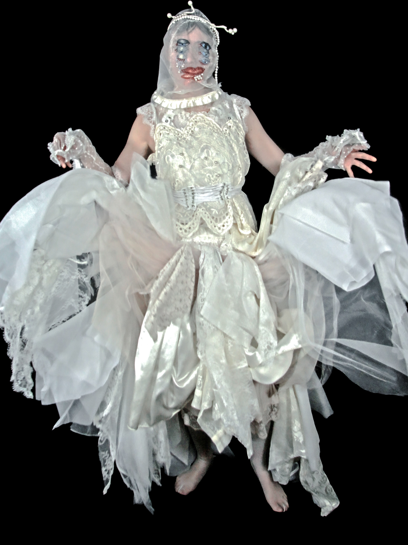 a figure wearing a dress made from lace scraps. It's a still of a video clip where she has tossed the skirt upward, so it looks like there's wind blowing it up or she's flying. She's wearing a sheer mask with six different eyes and a pair of lips cross-stitched on it, with pearl tears. Pearls also form a headband with a serotonin molecule as antenae.